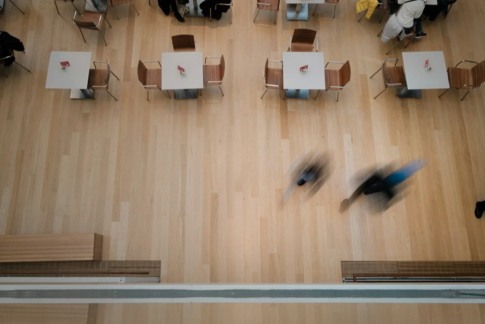 People crossing a room of small tables, blurred by motion, seen from above