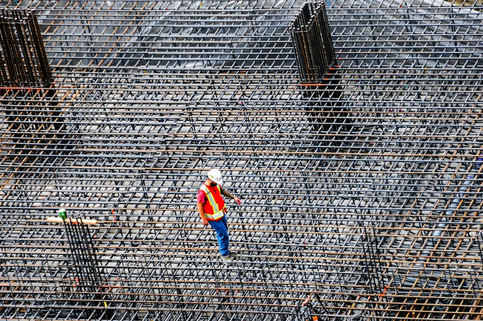 A construction worker in an orange vest inspecting rebar, seen from above